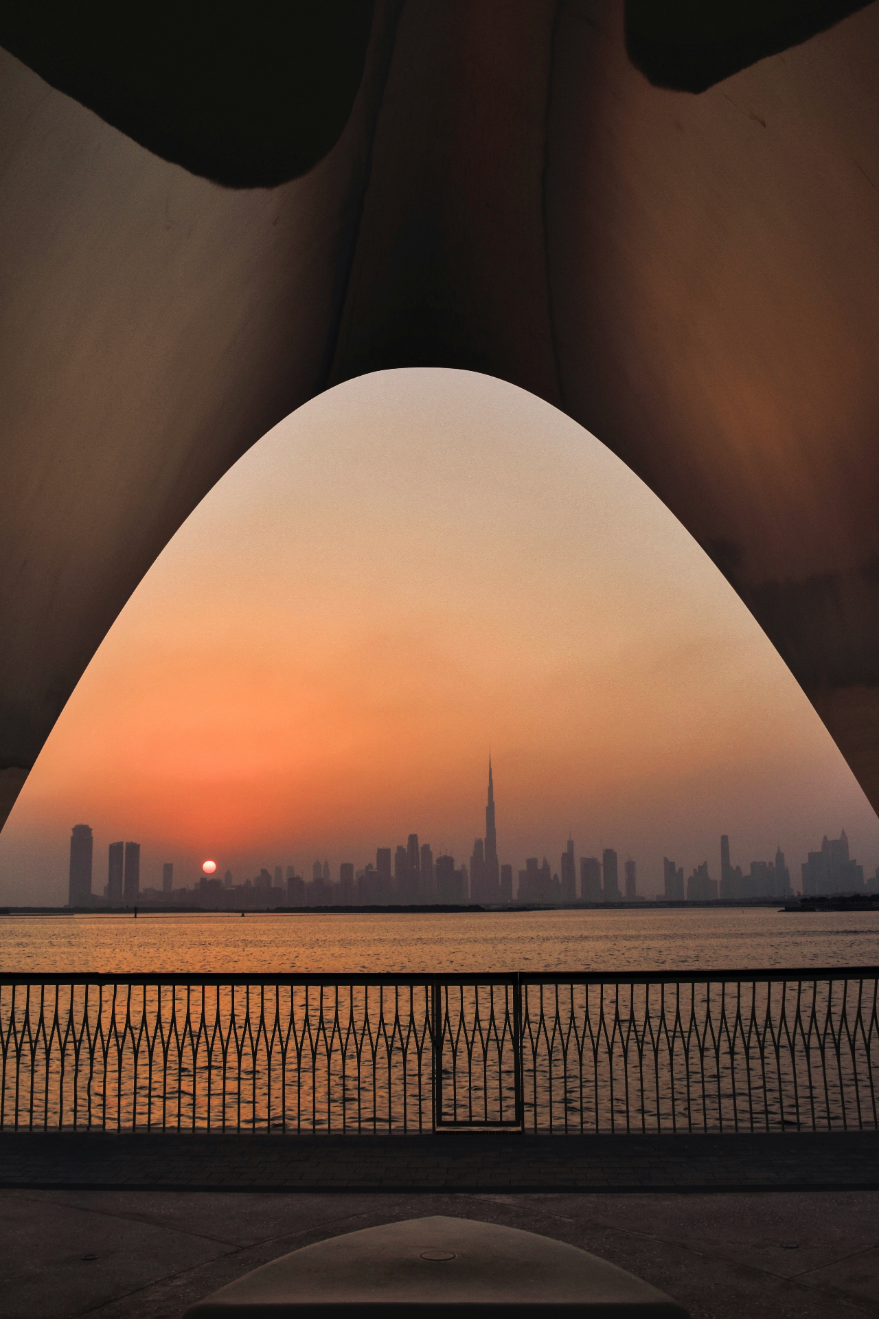 Oman skyline framed through an architectural arch at sunset with Sultan Qaboos Grand Mosque